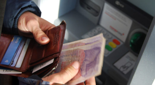 Close up of hands holding money in front of an ATM