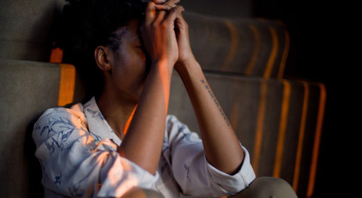 A women sits in darkness with her head in her hands